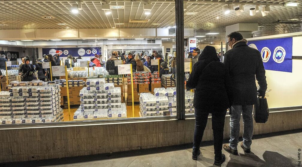 L'intérieur de la boutique Duralex d'Orléans. On voit de nombreux clients faire leurs achats, avec des étagères remplies de produits Duralex en verre, tels que des verres, plats et autres articles. L'ambiance semble animée avec de nombreuses personnes présentes dans le magasin.