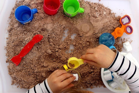 À la crèche de La Borde, les enfants jouent au sable magique sur des plateaux avec des ustensiles variés.